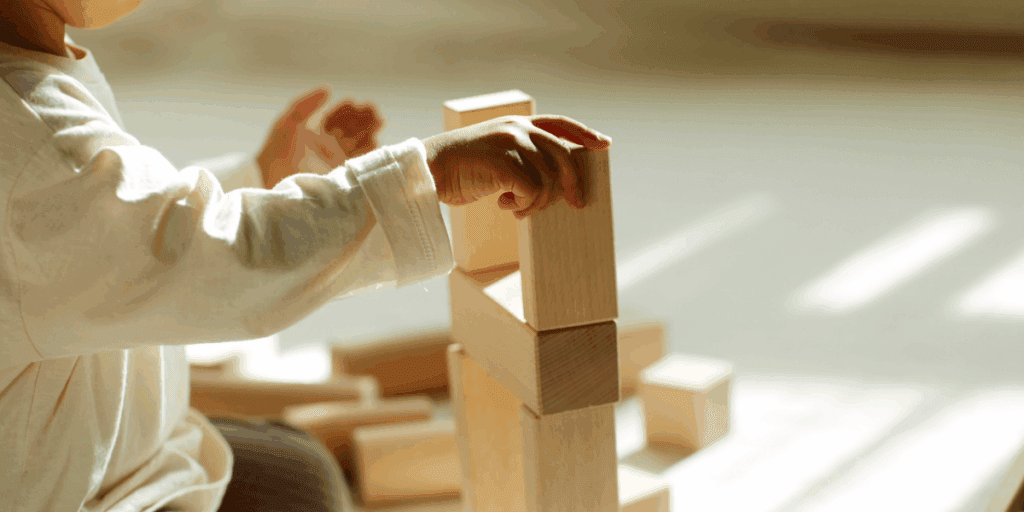 1 - SheSTEM Japan|教育×ジェンダー×共創で、未来を変える。 木製ブロックを積み上げて遊ぶ幼児の手元の写真。立体遊びを通して空間認識力・メンタルローテーションの土台が育つイメージ