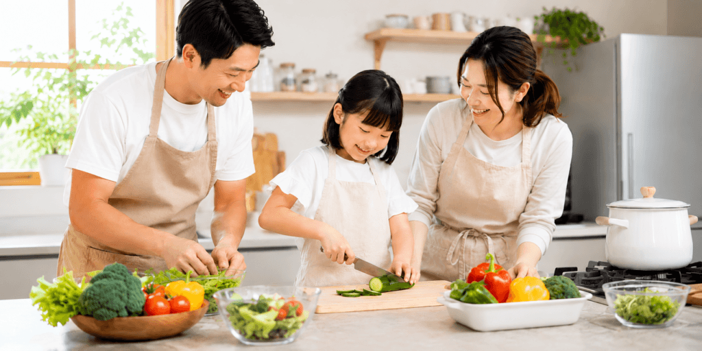 料理を通して実行ロジック機能と思考のOSを育む親子のキッチン風景。子どもが野菜を切り、父母が一緒に食事づくりを進めている。